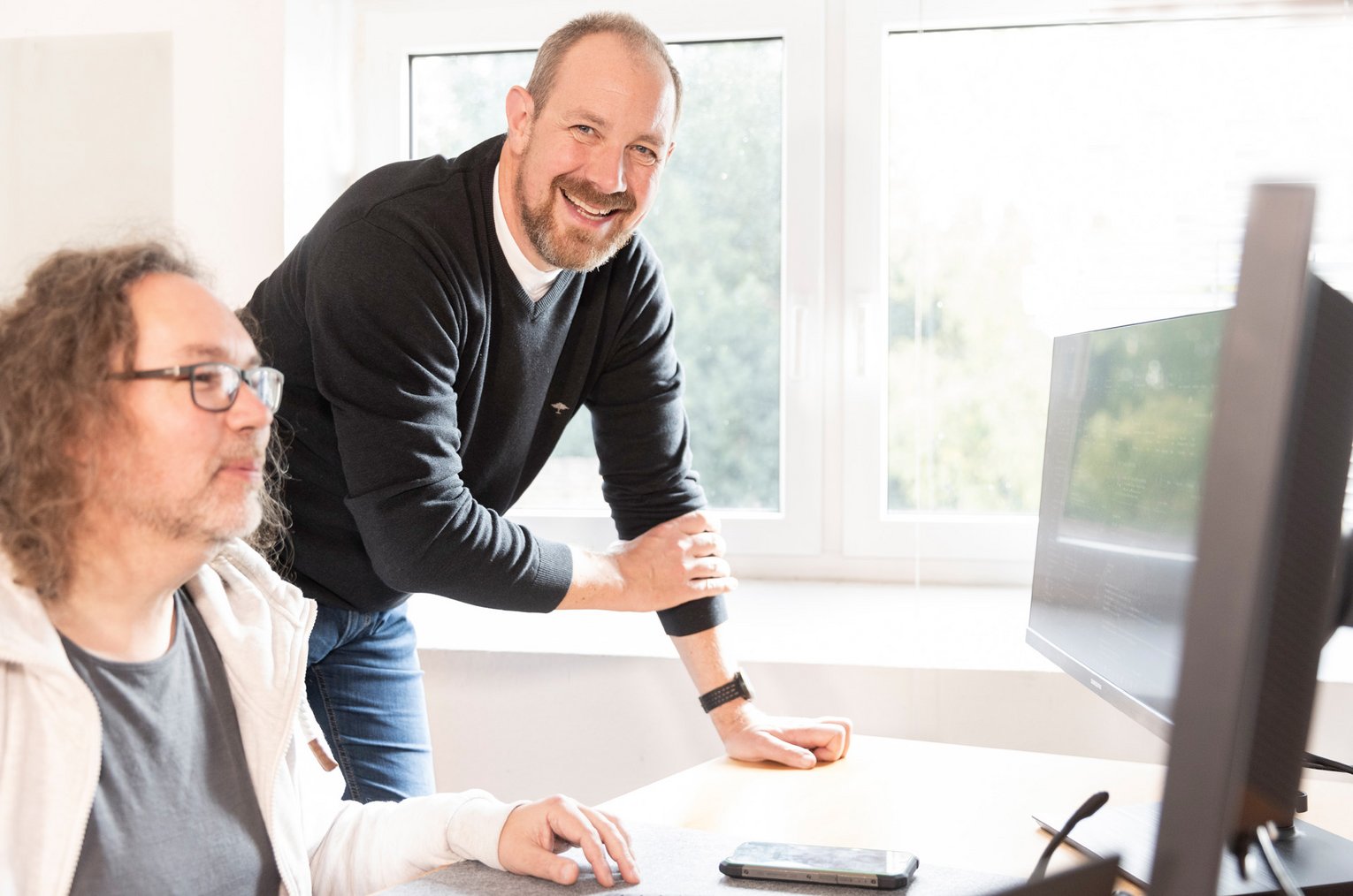Zwei Männer im Gespräch an einem Computermonitor